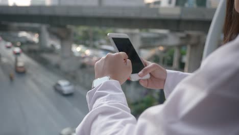 De-cerca-Mano-de-mujer-de-negocios-utilizando-el-teléfono-inteligente-en-el-centro-de-la-ciudad-moderna-en-la-noche-de-Bangkok-Tailandia.-Comunicación-Concept-Technology-por-teléfono-móvil