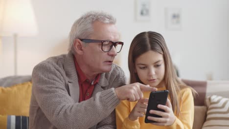 Abuelo-caucásico-enseñando-a-la-niña-cómo-utilizar-el-teléfono-inteligente