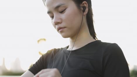 Attractive-caucasian-woman-athlete-running-using-a-smart-watch-checking-heart-rate-monitor-after-jogging-while-standing-beside-the-street-in-urban-city-sunset.