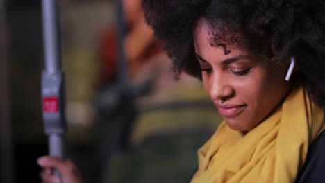 African-american-woman-with-earphones-holding-pole-travelling-on-public-bus