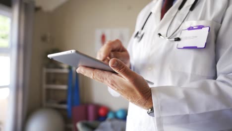 Close-up-of-male-doctors-hands-browsing-on-digital-tablet-in-consultation-room