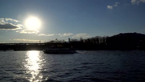 eine-romantische-Aussicht-auf-den-Fluss-bei-Sonnenuntergang-mit-Schiffen-und-Silhouetten-von-Menschen