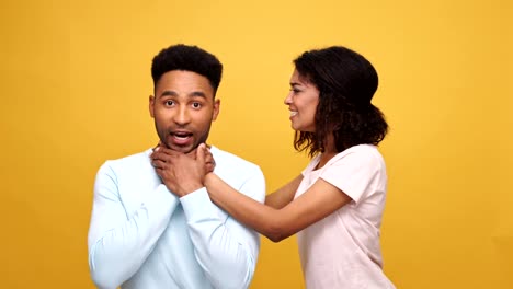 Violent-young-african-woman-strangling-her-boyfriend-isolated-over-yellow-background