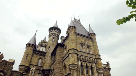 huge-gothic-building-in-summer-day,-camera-moves-through-branches-of-tree