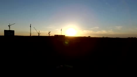 Aerial-shot-of-crans,-building-and-forest-at-sunset.