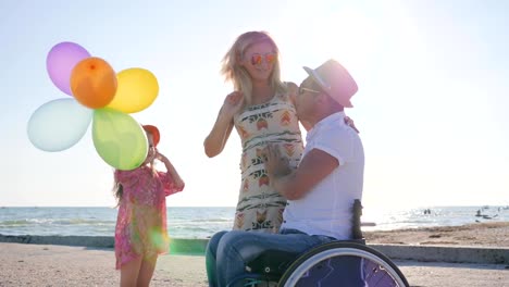 little-girl-listens-mother-and-father-with-handicap-in-wheel-chair-at-beach-in-summer-tim