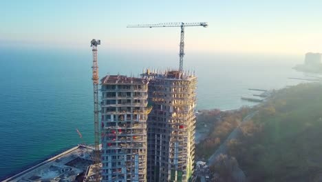 Aerial-Stadtansicht.-Bau-von-einem-Hochhaus-Wolkenkratzer-auf-dem-Ozean-durch-zwei-Kräne.-Die-Kamera-bewegt-sich-horizontal.-Geringere-Höhe-schießen