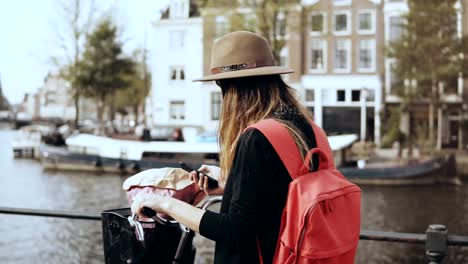 Cute-lady-with-bicycle-takes-photos-on-smartphone.-Young-Caucasian-female-journalist.-Amazing-old-town-architecture.-4K