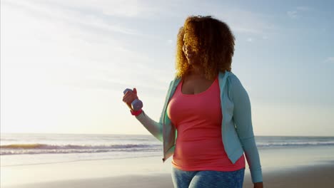 Ethnic-female-power-walking-with-dumbbells-at-sunset