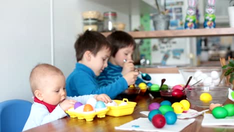 Three-children,-brothers,-coloring-and-painting-easter-eggs-at-home-in-kitchen-for-the-holiday