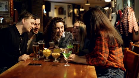 Group-of-friends-are-watching-something-funny-on-screen-of-smartphone,-discussing-it-and-laughing.-Modern-technology-in-everyday-life-of-young-people-concept.