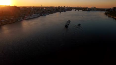 Barge-sails-along-the-river-near-the-city-port-on-sunset-aerial-footage