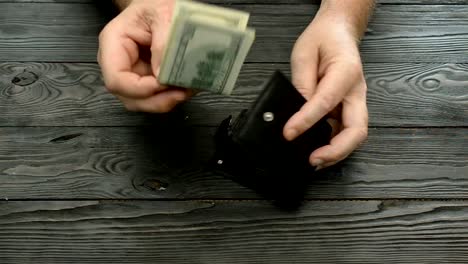 Man's-hands-count-the-US-dollars-and-cents,-banknotes-and-coins-from-a-black-leather-purse-over-a-dark-wooden-background.