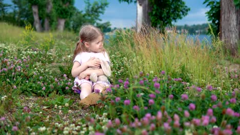 Ein-kleines-Mädchen-spielen-mit-einem-Spielzeug-Hasen-auf-der-Wiese-unter-den-blühenden-Klee