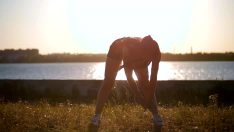 Sportliche-Frau-trainiert-den-Körper-vor-einem-Lauf-am-Meer-bei-Sonnenuntergang