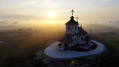 Luftaufnahmen-Video-der-kleinen-Dorfkirche-am-nebligen-Morgen.-Sonnenaufgangszeit.-Kyiv-Region,-Ukraine.-Fliegen-über-den-Fluss-Desna