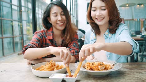 Beautiful-happy-Asian-women-lesbian-lgbt-couple-sitting-each-side-eating-a-plate-of-Italian-seafood-spaghetti-and-french-fries-at-restaurant-or-cafe-while-smiling-and-looking-at-food.