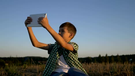 muchacho-hablando-por-video-llamada-en-tablet-sentado-en-el-campo-al-atardecer