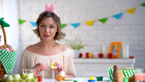 Smiling-woman-having-fun-holding-colorful-Easter-eggs-near-her-eyes,-joke