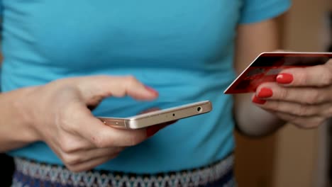 Frau-in-einem-blauen-Hemd,-die-Online-Zahlung-mit-Kreditkarte-und-Smartphone,-Online-shopping,-Lifestyle-Technologie.-Mädchen-tritt-die-Kreditkartennummer-in-das-Smartphone.-Closeup.-Hautnah.