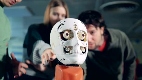 Men-and-woman-talk,-checking-a-robotic-head,-close-up.