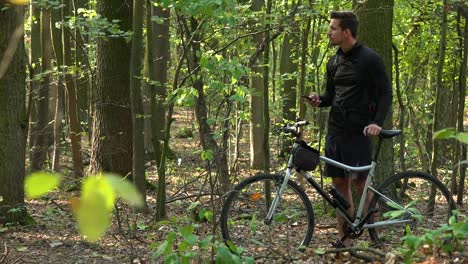 Ein-Radfahrer-steht-mit-einem-Fahrrad-in-einem-Wald-und-arbeitet-auf-einem-Smartphone