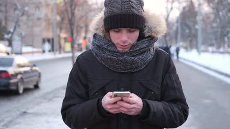 Man-walking-on-street-in-warm-clothing-and-text-messaging-on-mobile-phone