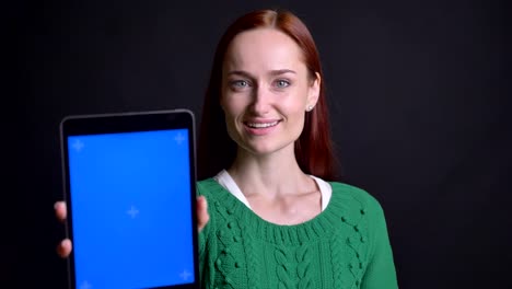 Closeup-portrait-of-attractive-caucasian-female-scrolling-down-on-the-tablet-and-showing-its-screen-to-camera-smiling