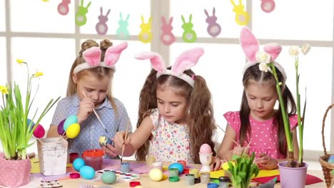 Niños-felices-usando-orejas-de-conejo-pintando-huevos-el-día-de-Pascua.