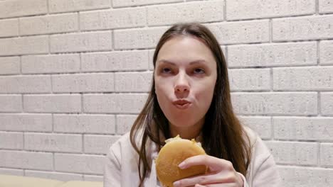 Woman-eating-a-hamburger-with-relish-and-delight-in-cafe.