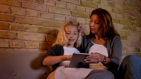 Closeup-Shoot-von-jungen-kaukasischen-Mutter-und-ihre-kleine-hübsche-Tochter-mit-dem-Tablet.-Mama-fixiert-ihre-Mädchen-Haare-mit-Zärtlichkeit