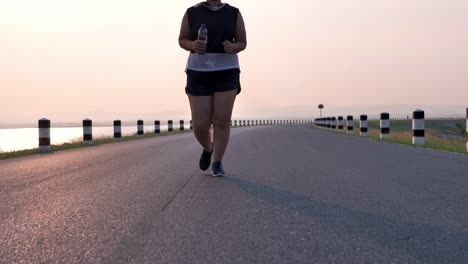 Übergewichtige-asiatische-Frauen-joggen-am-frühen-Morgen-im-Sonnenlicht-auf-der-Straße.-Konzept-des-Gewichtsverlustes-mit-Bewegung-für-die-Gesundheit.-Langsame-Bewegung,-Bottom-Ansicht