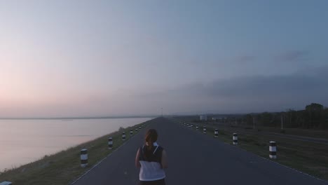 Asiatische-Frauen-joggen-in-der-Straße-am-frühen-Morgen-Sonnenlicht-am-Wasserspeicher-Pa-Sak-Jolasid-Dam.-Konzept-des-Gewichtsverlustes-mit-Bewegung-für-die-Gesundheit.-Langsame-Bewegung,-Rückansicht