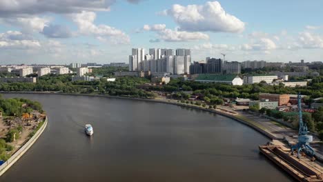 Vista-aérea-del-puente-ferroviario,-con-un-tren-en-movimiento-en-él,-a-través-del-río-que-fluye-a-través-de-una-ciudad-importante