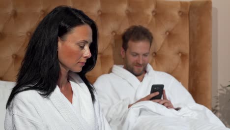 Mature-woman-looking-unhappy-while-her-husband-texting-on-smart-phone