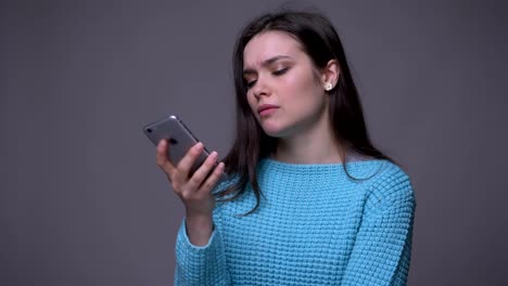 Closeup-shoot-of-young-pretty-brunette-female-texting-on-the-phone-with-background-isolated-on-gray