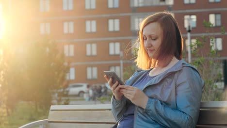 Frau-mit-Smartphone-auf-Bank-in-der-Stadt-sitzen