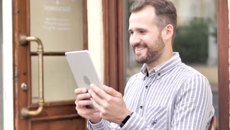 Young-Man-Watching-Video-on-Tablet-while-Sitting-Outdoor