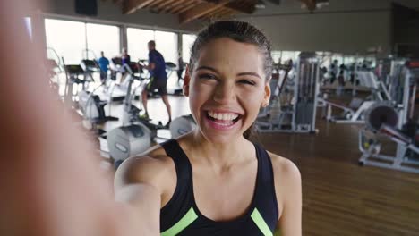 Una-mujer-en-el-gimnasio-toma-una-foto-para-enviar-a-amigos-o-poner-en-las-redes-sociales-y-toma-la-foto-mientras-sonríe.