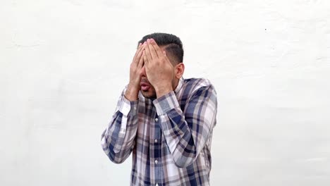 I-don't-want-to-look-at-this.-Portrait-of-shocked,-confused,-scared-or-shyed-bearded-man-in-blue-shirt-standing-and-closed-his-eyes-with-hands.