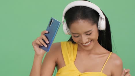 Asian-beautiful-woman-listening-music-online-and-happy-emotion-smile.-Woman-wearing-headphone-and-hold-smartphone.-Concept-of-beauty,-fashion-and-music-experience.