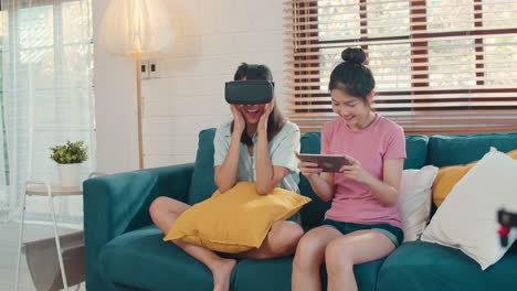 Junge-asiatische-Lesbische-Paar-mit-Tablet-und-Virtual-Reality-spielen-Spiele-zusammen,-während-liegen-Sofa-im-Wohnzimmer-zu-Hause.