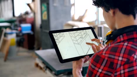 Woman-looking-at-tablet-screen-checking-furniture-design-in-wood-workshop