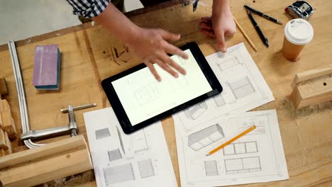 Male-hand-touching-tablet-screen-with-technical-drawing-of-furniture-in-workshop