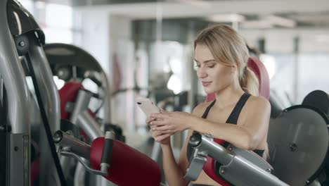 Fitness-mujer-relajarse-con-el-teléfono-móvil-en-el-gimnasio-deportivo.