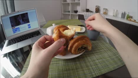 POV-von-Frau-Essen-Croissant-und-Watching-Serie-auf-Laptop