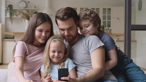 Padres-felices-con-niños-divirtiéndose-usando-el-teléfono-inteligente-en-casa