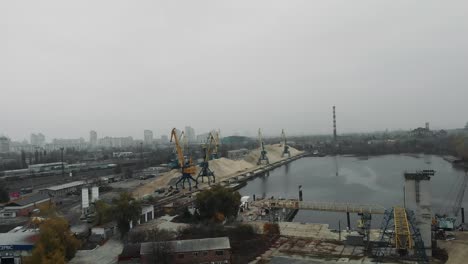 Industrial-part-of-the-city.-Construction-cranes-and-smokestacks-at-manufacturing-plant.-Transporting-of-sand.-Piles-of-sand-at-plant,-aerial-drone-view