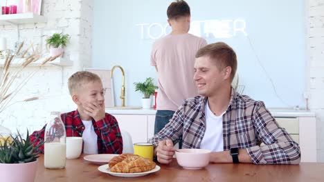 Feliz-familia-gay-dos-padres-e-hijo-están-desayunando-en-la-cocina.