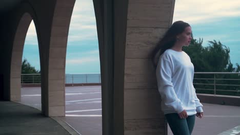 Beautiful-girl-with-long-hair-and-a-white-sweatshirt,-standing-under-one-of-several-arches-of-the-building.